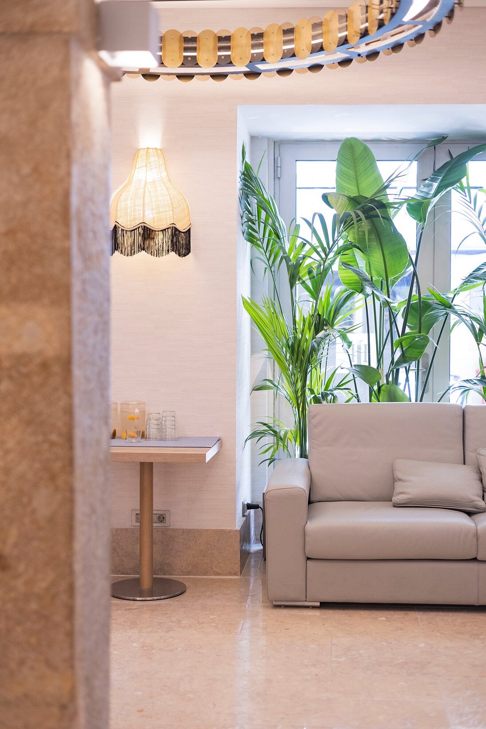 Zona lounge del Hotel Santa Justa en Lisboa con lámpara de pared artesanal, luz cálida, sofá y plantas decorativas en un ambiente elegante.
