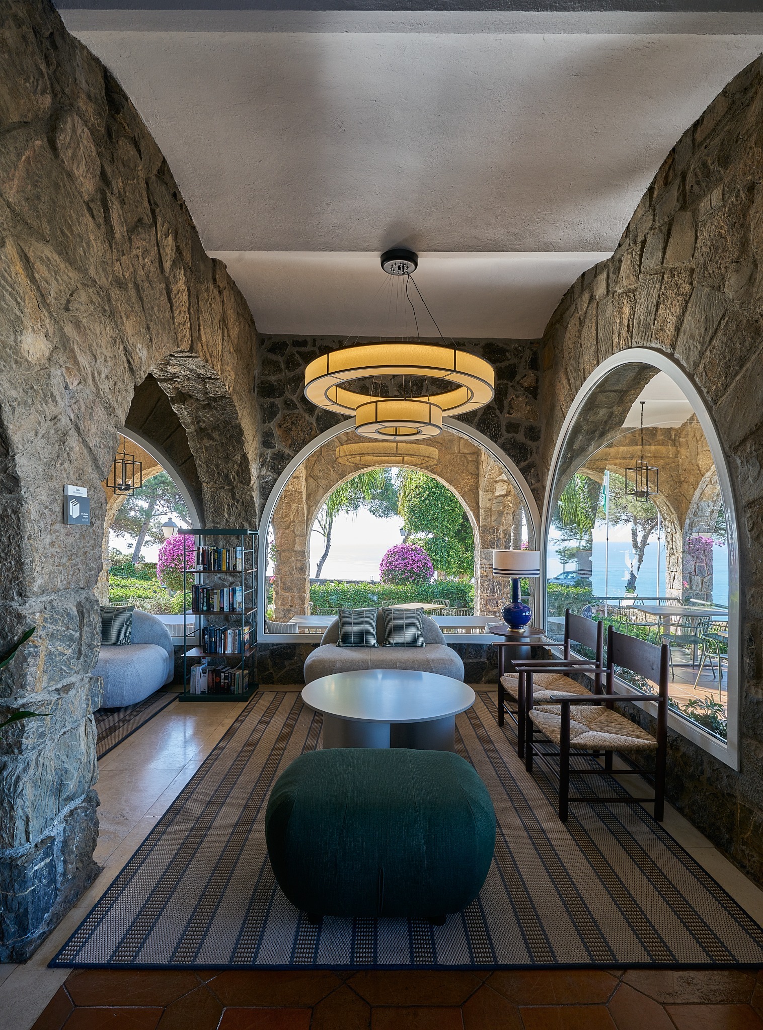 Zona lounge del Parador de Málaga Gibralfaro con lámpara circular suspendida, arcos de piedra y vistas al mar.