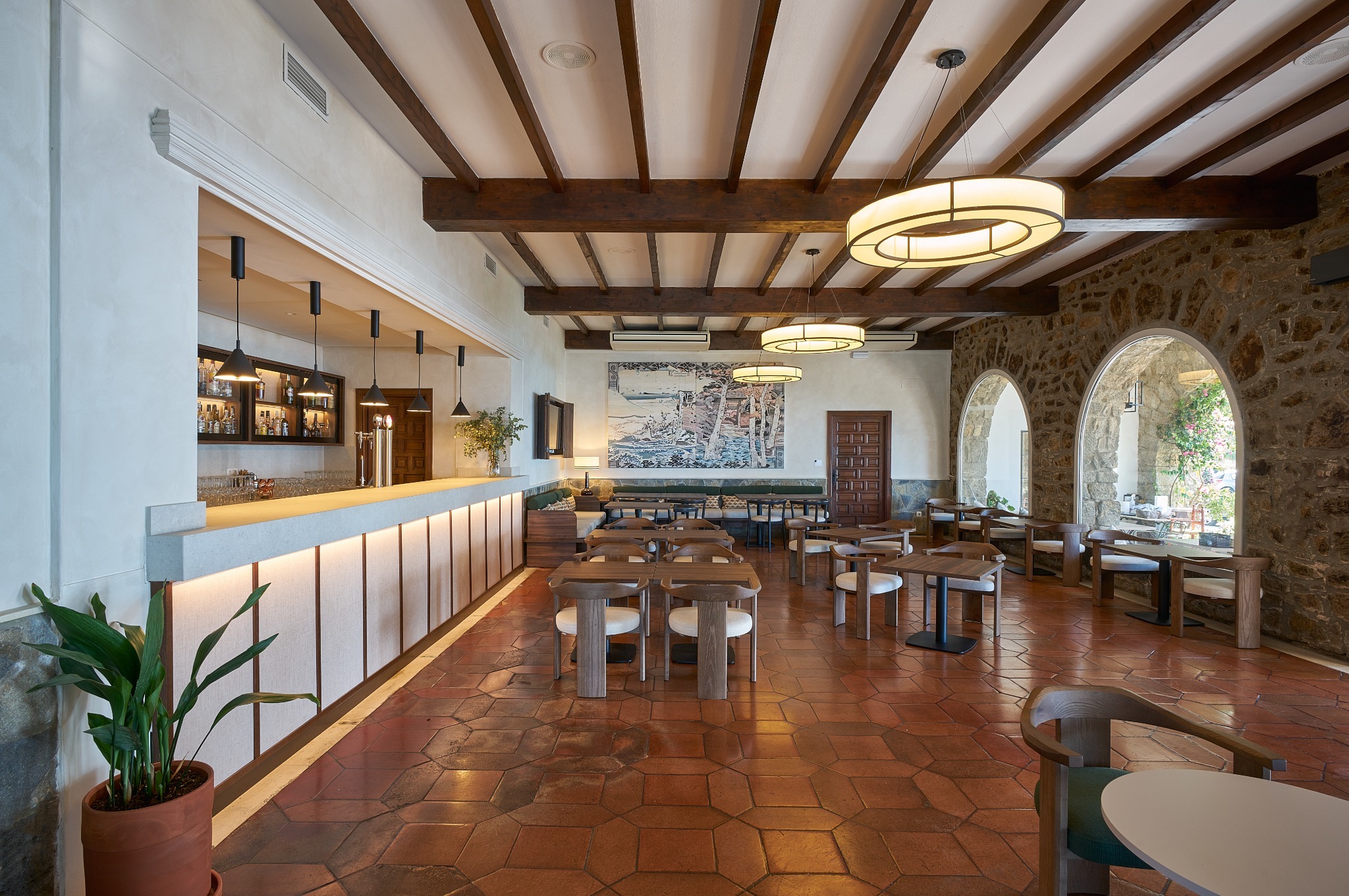 Zona lounge del Parador de Málaga Gibralfaro con lámpara circular suspendida, arcos de piedra y vistas al mar.