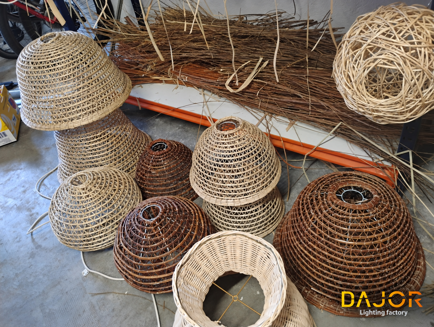 Pantallas de mimbre de diferentes tamaños y tonos agrupadas en el taller junto a haces de fibras y materiales de cestería.