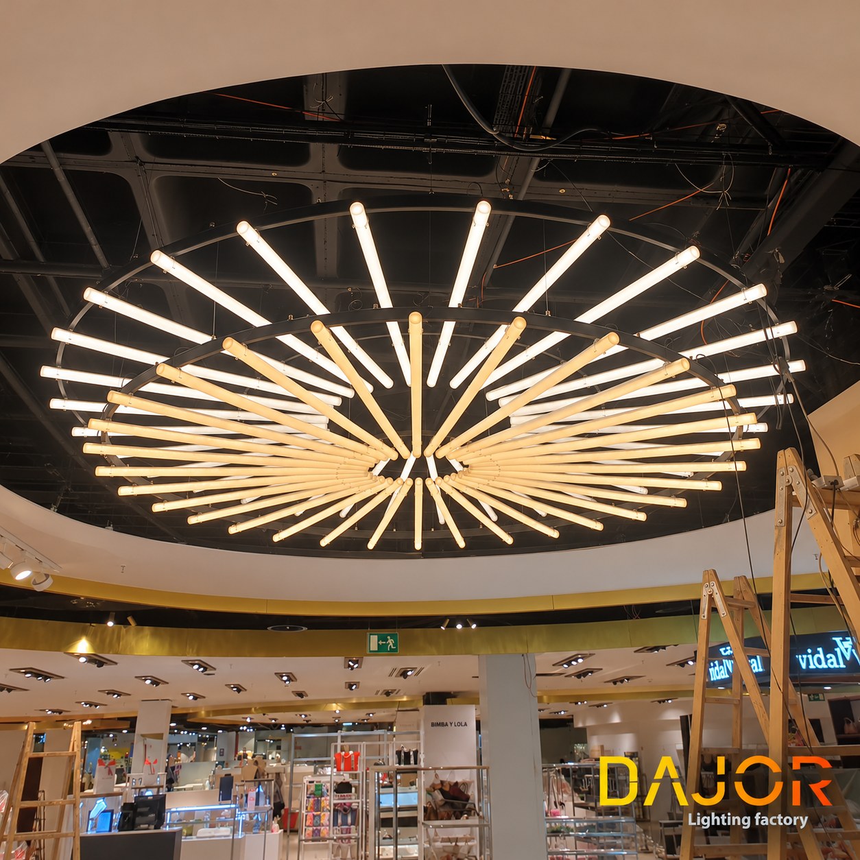 Luminaria circular encendida durante su instalación en El Corte Inglés Castellana, con escaleras de montaje a los lados.