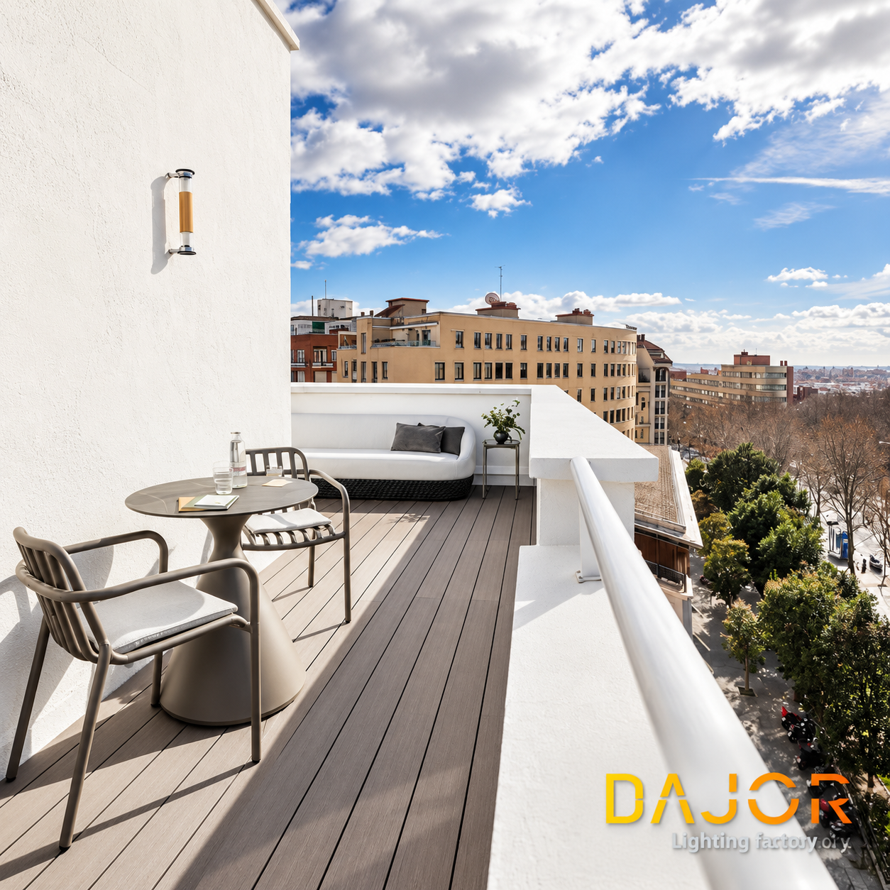 Terraza urbana de hotel con mesa, sillas, sofá exterior y aplique de pared sobre una fachada blanca.