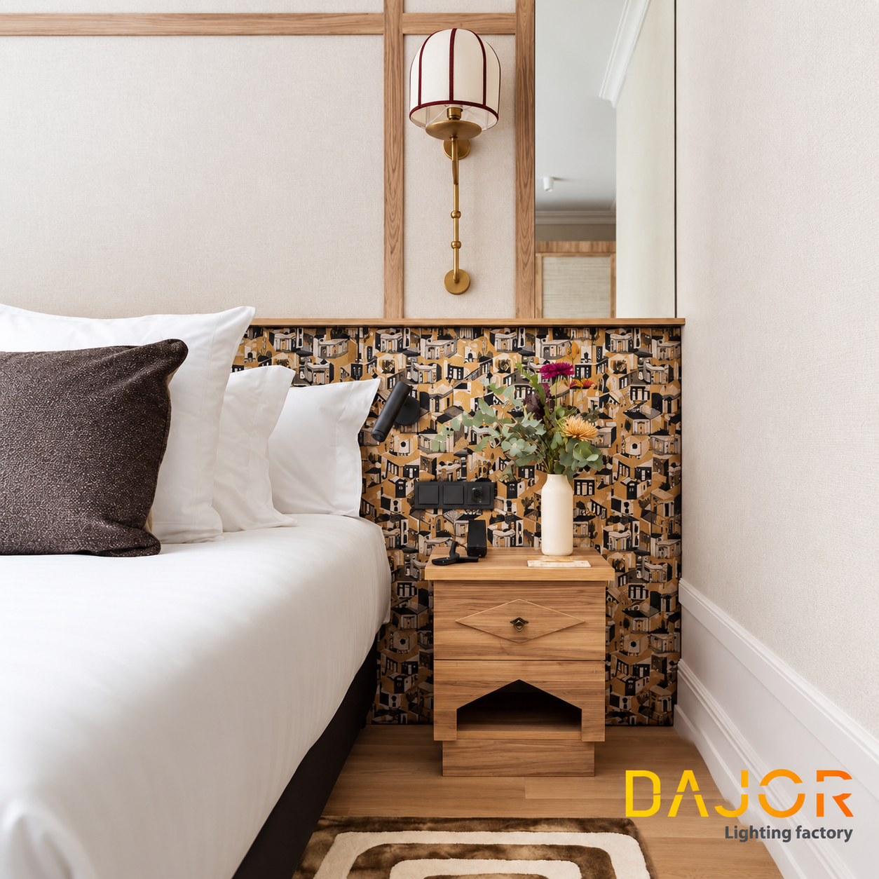 Detalle de habitación de hotel con aplique de pared de pantalla textil blanca con ribetes rojos y estructura en acabado dorado junto a la cama.