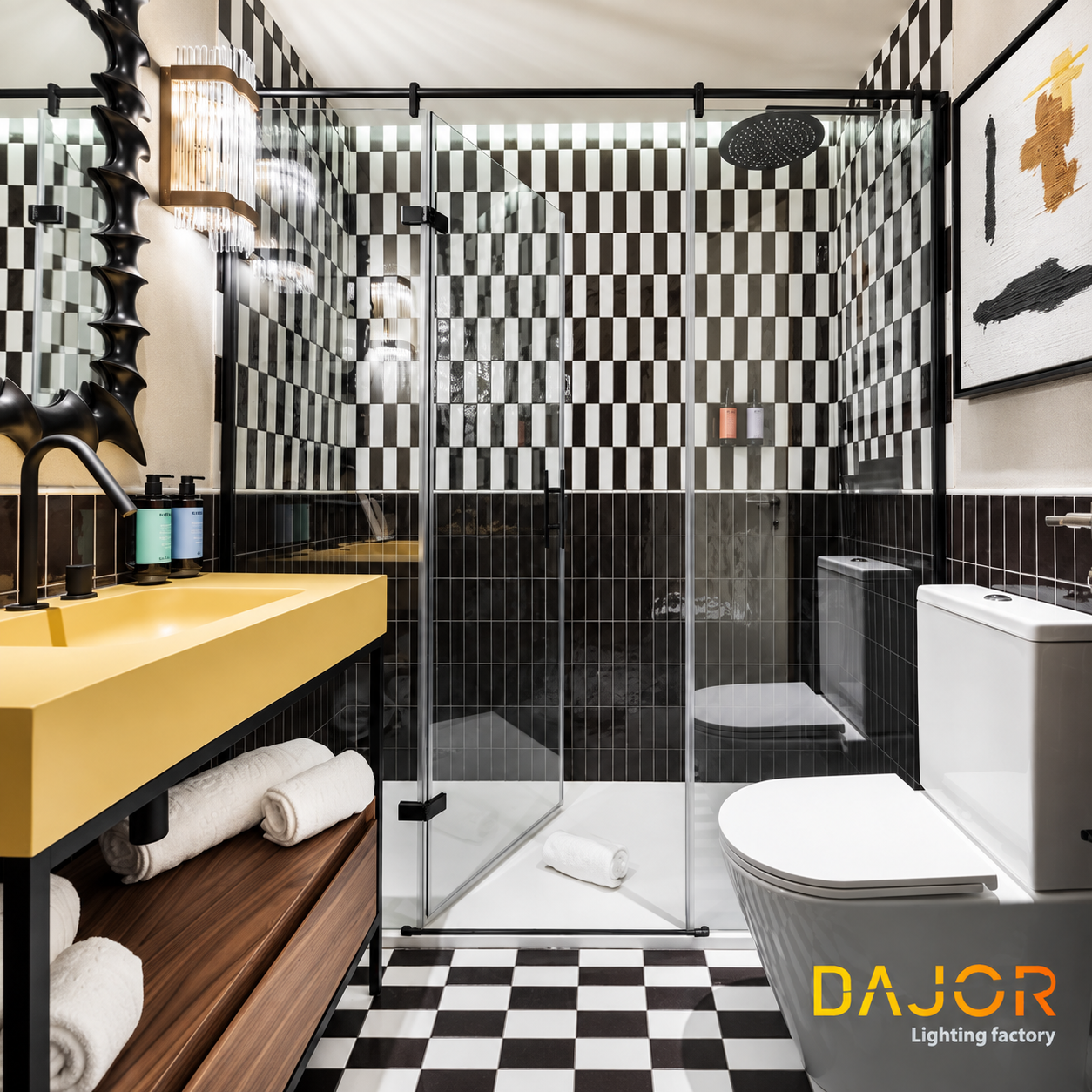 Baño de hotel con azulejos blancos y negros, lavabo amarillo, ducha de cristal y aplique decorativo de cristal junto al espejo.
