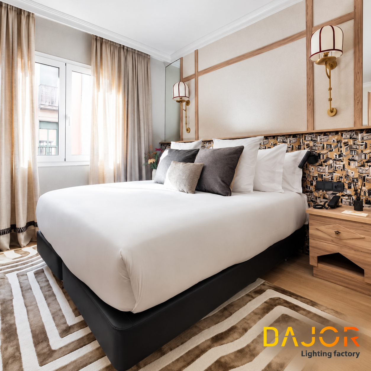 Habitación de hotel luminosa con cama doble, cabecero decorativo de madera y dos apliques de pared con pantalla textil blanca y detalles rojos.