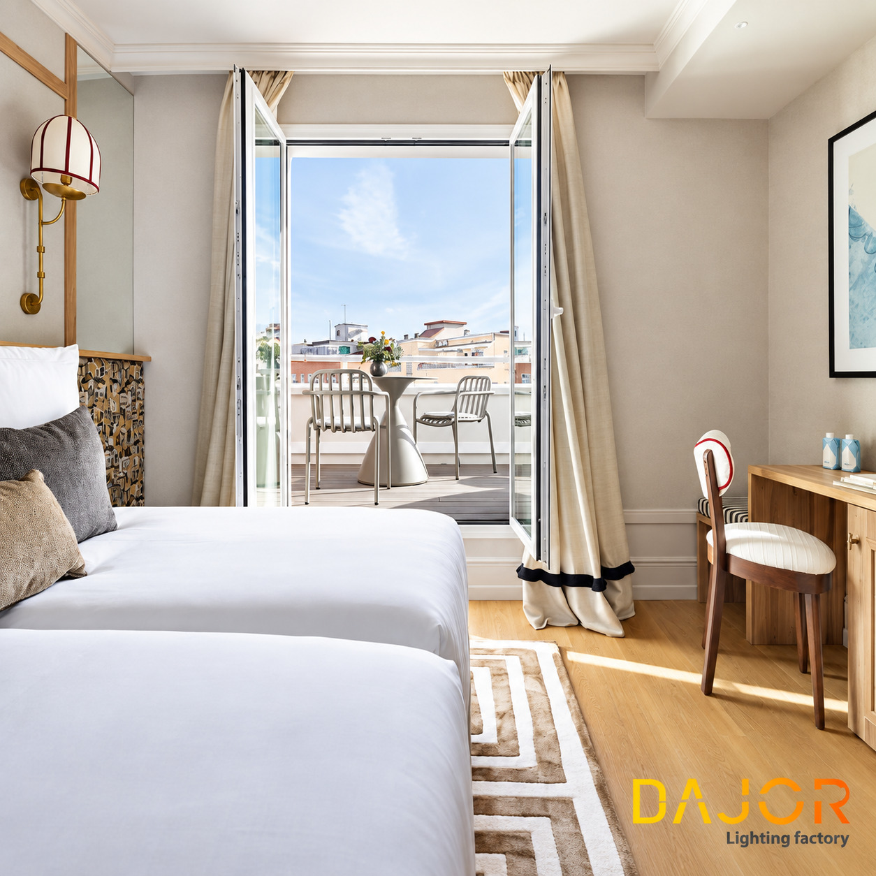 Habitación de hotel con dos camas, escritorio, aplique decorativo y puertas abiertas hacia una terraza exterior amueblada.